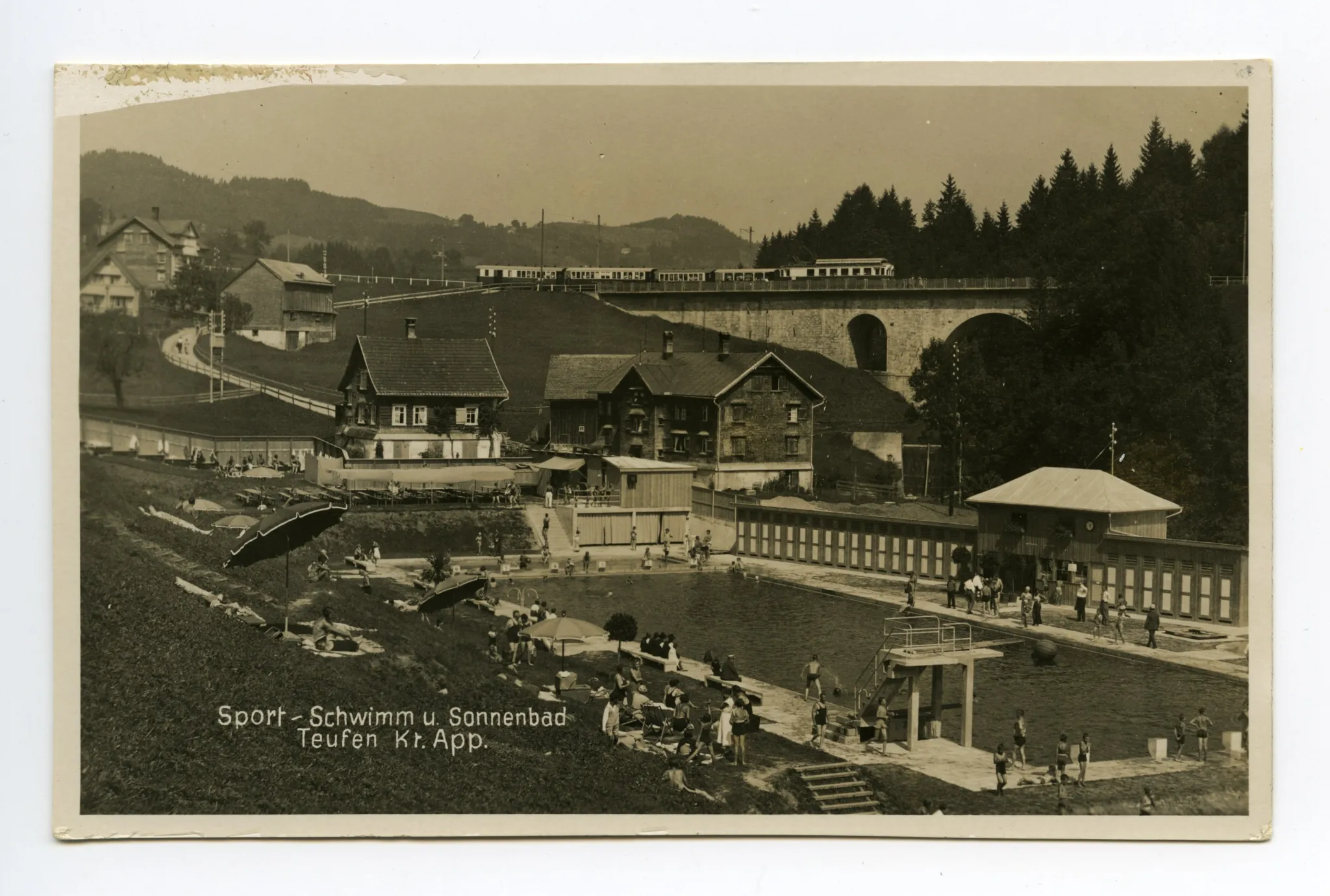 mit Badegästen, alte Bahnbrücke und vorbeifahrender Zug im Hintergrund