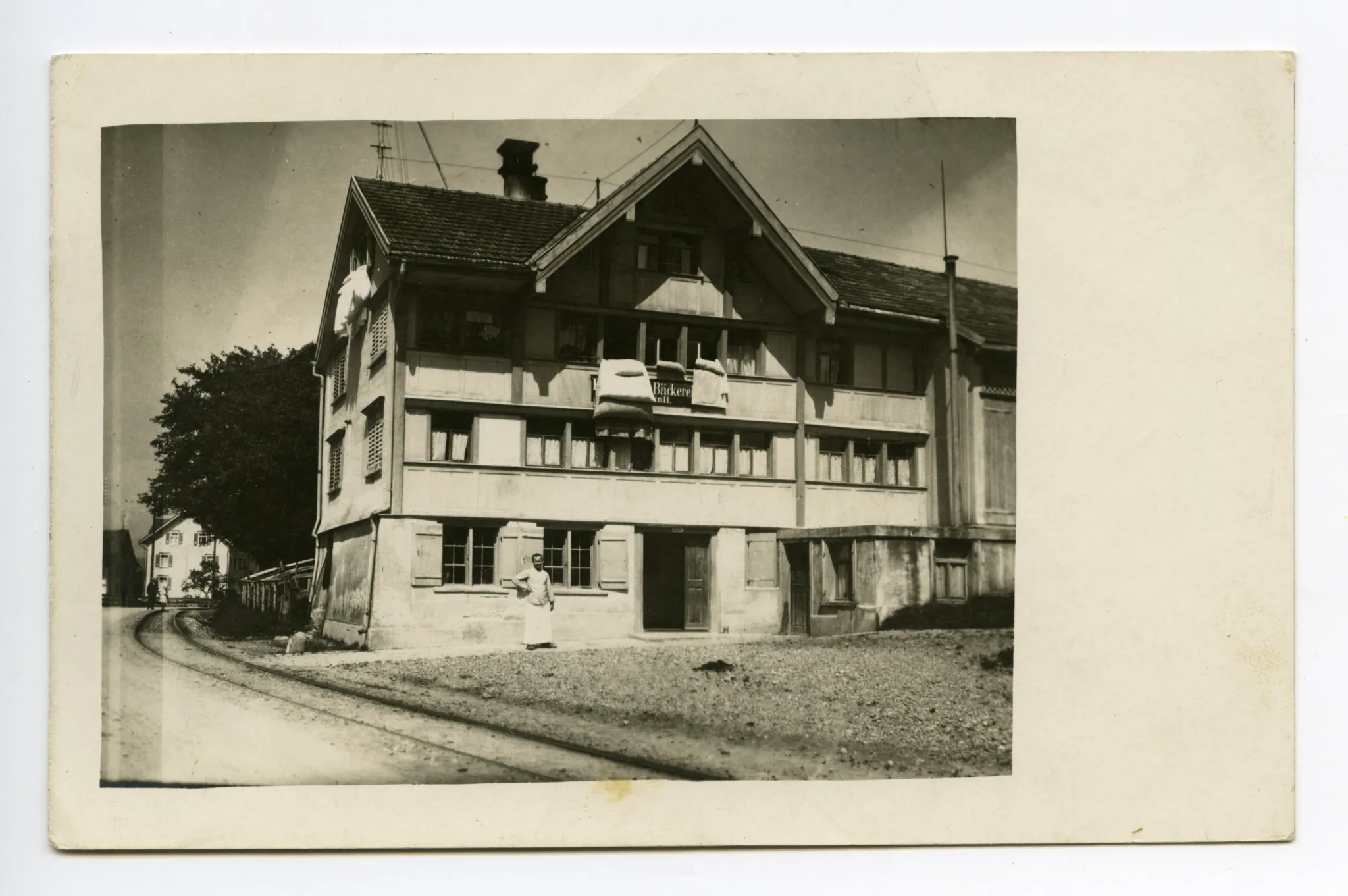 abgebrochen 1977, Ansicht mit Person vor dem Haus und Bahnschienen