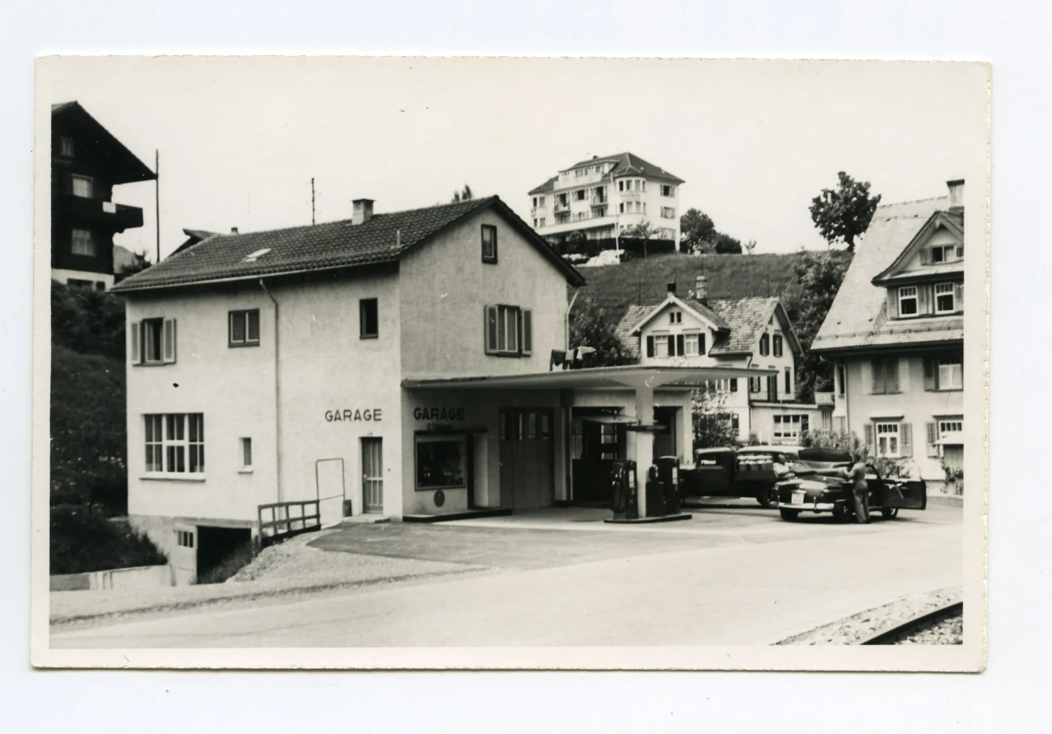 Ansicht Garage mit Tankzapfsäulen und Autos, sowie Milchwagen