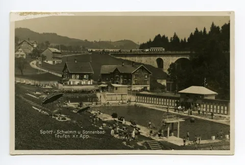 mit Badegästen, alte Bahnbrücke und vorbeifahrender Zug im Hintergrund