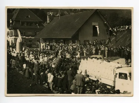 3 Wagen hintereinander: Lastwagen der Haslen-Mühle?, Fuhrwerk der Obst- und Gemüsebauern, Konditoren mit ihrer „Riesenpraline“, im Hintergrund Güterschuppen und Bahnhof