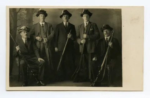 Gruppenbild der Jäger in Anzug und geschmücktem Hut und Jagdflinte